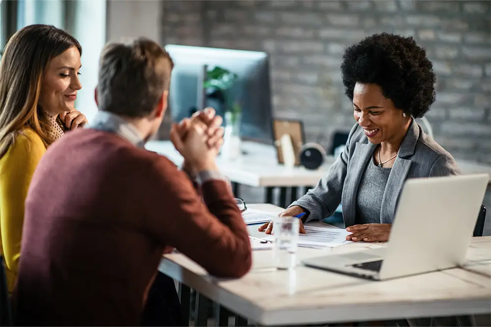A smiling lawyer reviews documents with a couple in a modern office, symbolizing the benefits of hiring a prenup lawyer over using online templates.