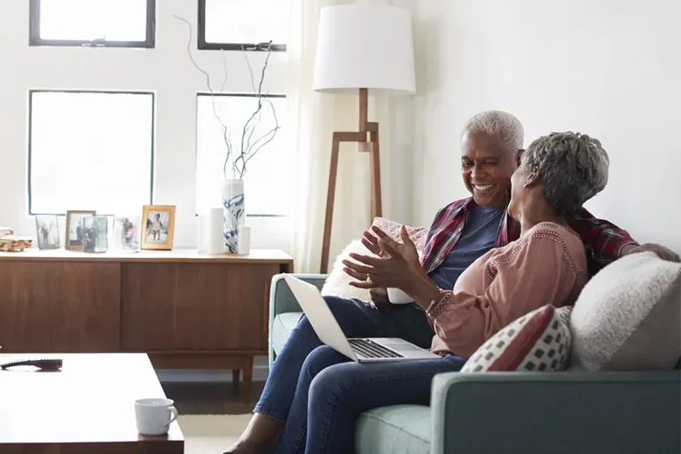 A joyful older couple sitting on a couch with a laptop, discussing plans together—symbolizing the importance of financial and legal protection when planning to remarry later in life.
