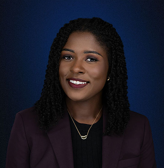 Professional headshot of LaSheena M. Williams, Esq., smiling in a plum blazer against a blue gradient background.
