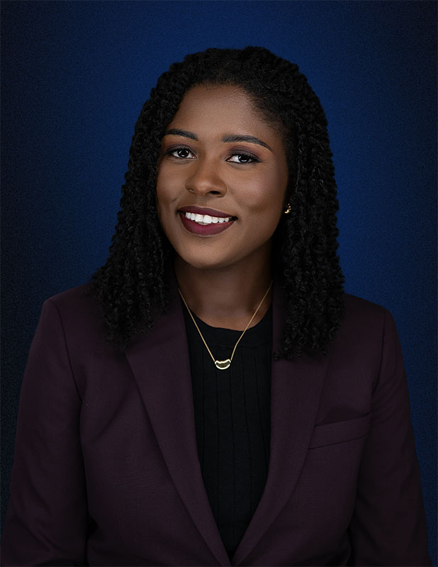 Professional headshot of LaSheena M. Williams, Esq., smiling in a plum blazer against a blue background.